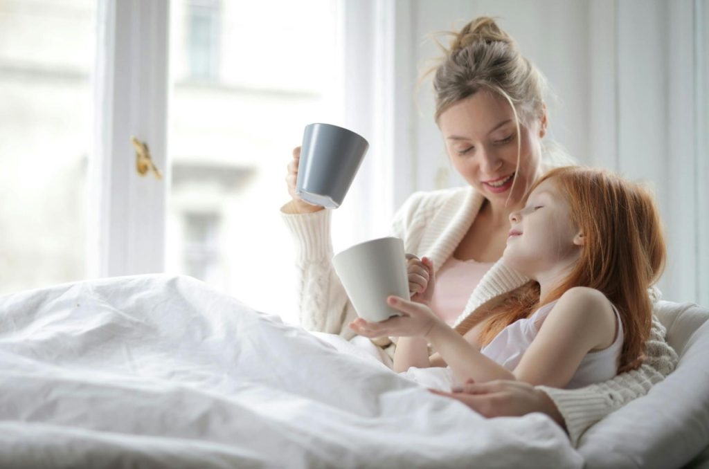Woman and daughter in a cozy sweater reading a book on a comfortable couch in a heated room
